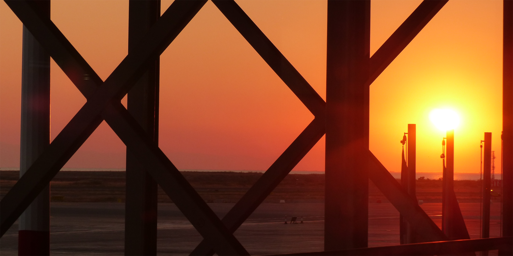 Hinter eine Metallkonstruktion ist Rollfeld welches von den rot-gelben Lichtern des Sonnenuntergangs erleuchtet wird.